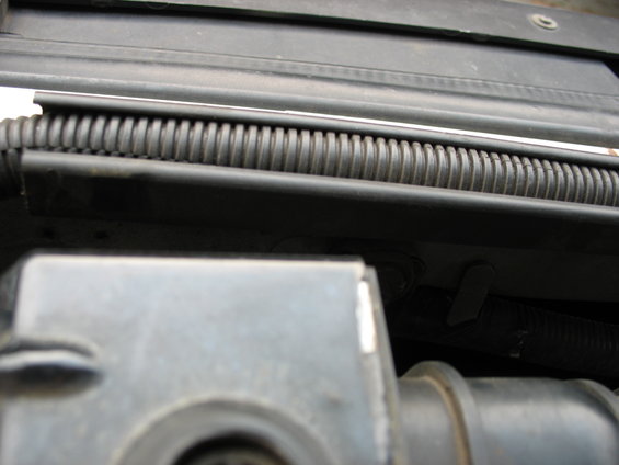 Close-up of a black corrugated hose above gray engine components