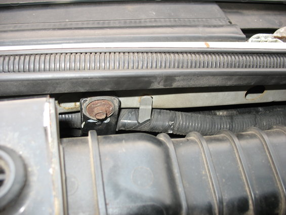 Engine bay part with rusted bolt and black hose