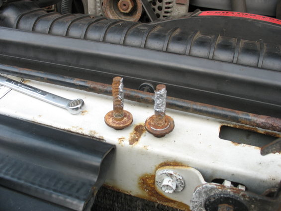 Two rusty bolts and a wrench on a white surface near a black grille