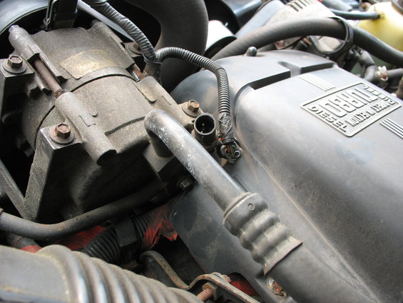 Engine bay with AC compressor and black plastic engine cover with "DIESEL" text