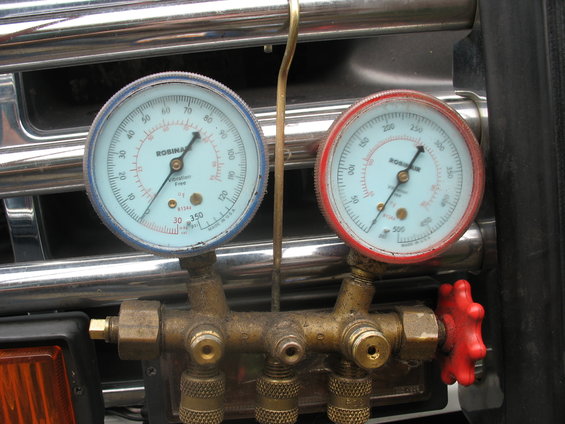 AC manifold gauge set with blue and red gauges mounted in front of a chrome grille