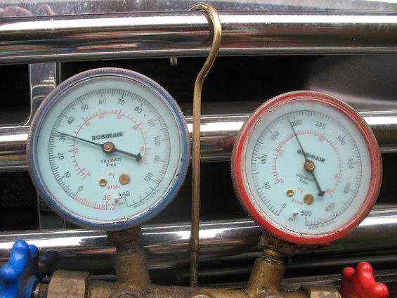 Robinair AC manifold gauges with blue and red handles, attached to a chrome grille