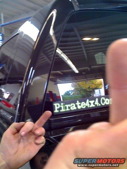 Sticker on a black vehicle reads "Pirate4x4.Com". A hand is giving the middle finger