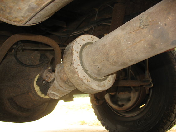 Close-up of a vehicle's driveshaft connecting to the differential, with a tire visible