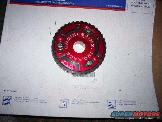 Red aluminum timing gear with black teeth and silver bolts, labeled "ENGINEERING INC. RACE"
