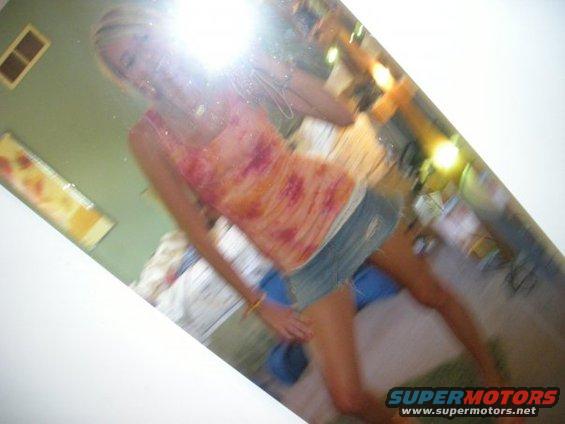 Woman in a tie-dye top and denim shorts takes a mirror selfie