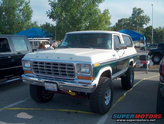 1979 Ford Bronco with green and white paint, lifted suspension, and aftermarket wheels. Other vehicles and tents are visible in the background