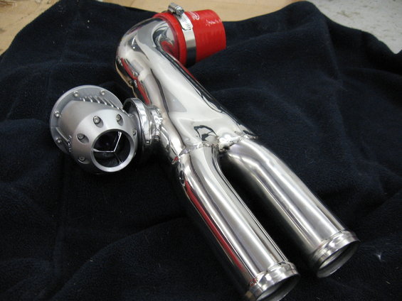 Shiny metal turbo blow-off valve connected to chrome piping with a red silicone coupler