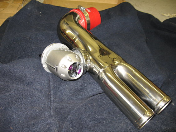 Silver turbocharger bypass valve with purple blades attached to polished chrome exhaust piping with a red silicone coupler