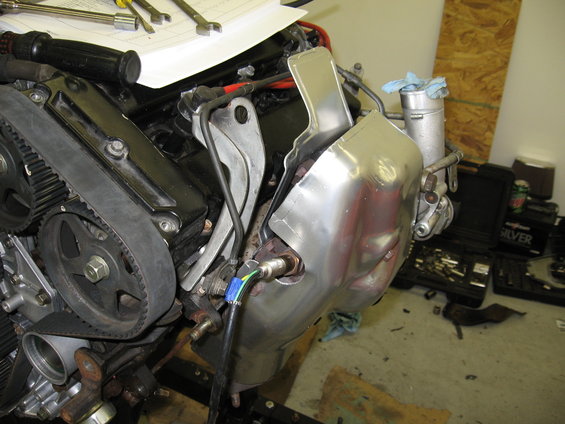 Engine timing belt and pulley assembly with a shiny metal shield covering part of the exhaust manifold
