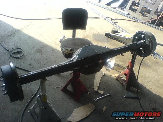 Rear axle assembly on jack stands, with a chair behind it. Tools and scrap metal are on the floor