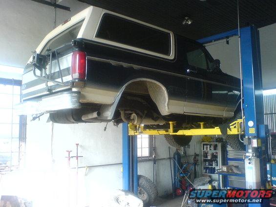 Side view of a black and white 1985 Ford Bronco on a lift in a garage