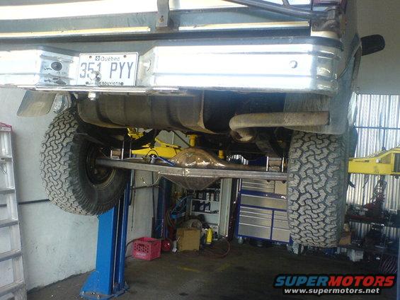Rear axle, suspension, and fuel tank of a vehicle on a lift. Quebec license plate 351 PYY is visible