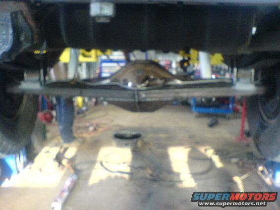 Underside view of a vehicle's rear axle and suspension components, possibly in a garage or repair shop