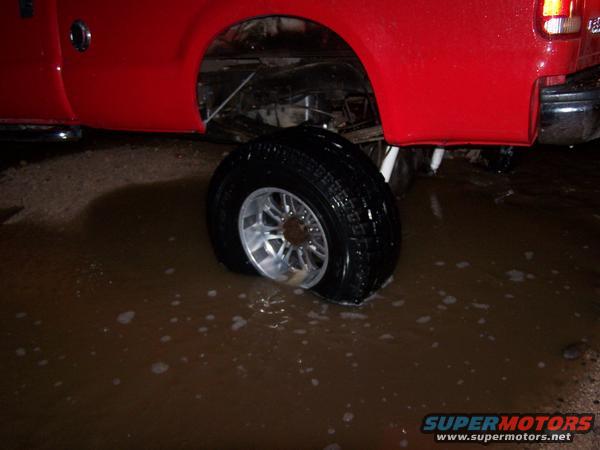 Red truck rear wheel stuck in muddy water, chrome rim visible
