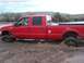1991 Ford Bronco - Red Ford F-250 Super Duty pickup truck is stuck in mud, showing its lifted suspension and aftermarket wheels.