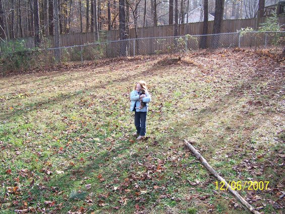 Kid holding a puppy in a backyard with a fence and trees. Date stamp in corner