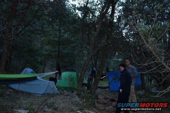 Campsite with tents, a hammock, and two people standing near a fire pit