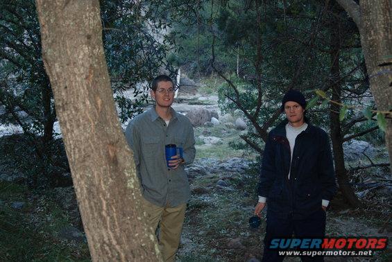 Two men in a wooded area, one holding a blue cup