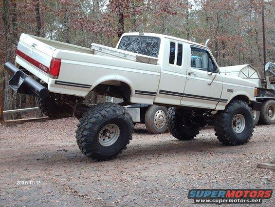White Ford F-150 pickup truck with oversized tires and lifted suspension, seen from the side