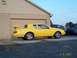 1986 Mercury Cougar - A yellow coupe with a distinctive rear spoiler is parked outside a building, with other vehicles visible in the background.