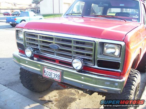 Red 1986 Ford Bronco front end with chrome grille, auxiliary lights, and California plate 5GOE398