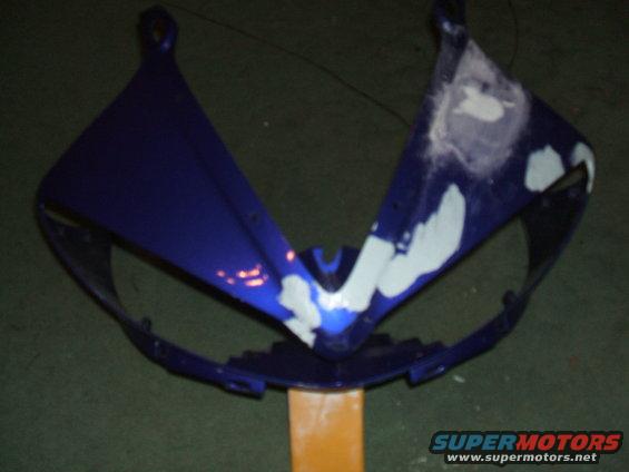 Blue motorcycle fairing with white primer spots, mounted on an orange stand