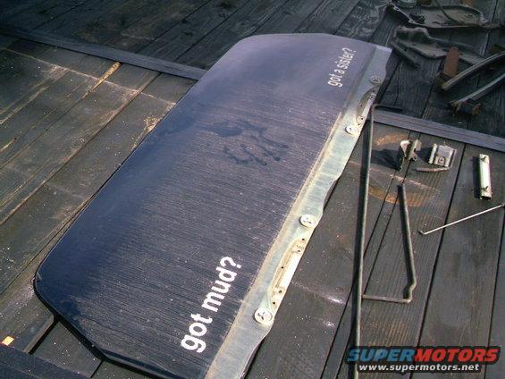 Dark blue car door with white text "got mud?" and "got a sister?", lying on a wooden surface with tools