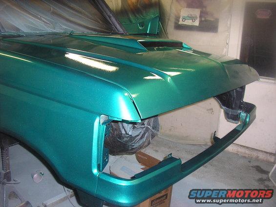 Green metallic SUV front end, hood scoop, missing headlights, on jack stands