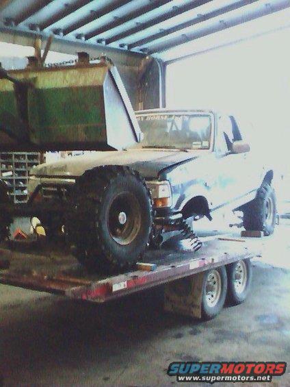 1992 Ford Bronco on a trailer, front left tire is oversized, body is dark blue with some green paint splatter