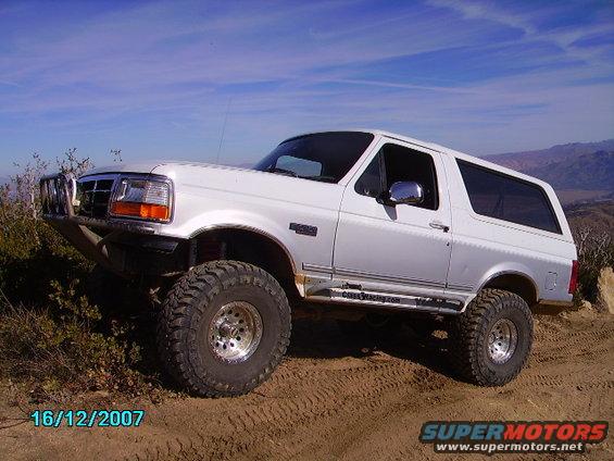 White 1990s Ford Bronco with aftermarket bumper and large tires on a dirt trail