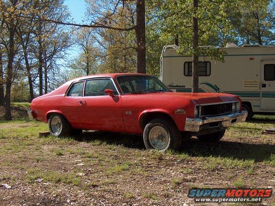 Red coupe parked outside with trees and a camper behind it. SS badge on fender