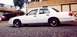 1999 Ford Crown Victoria - A white sedan is parked on a gravel lot in front of a building.