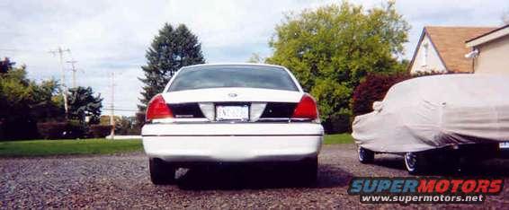 White 1998 Ford Crown Victoria rear view, license plate visible, parked on gravel next to a car covered in a tarp