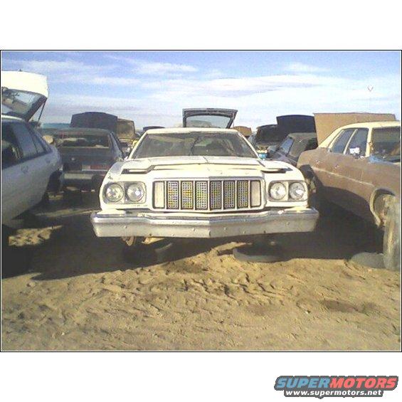White 1972 Ford Gran Torino front end in a junkyard, grille is prominent, headlights are round, car is elevated on tires