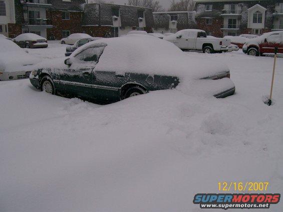 Side view of a dark green sedan buried in snow
