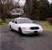 1999 Ford Crown Victoria - A white 1999 Ford Crown Victoria is parked on a gravel driveway in front of a house.