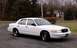 1999 Ford Crown Victoria - This white 1999 Ford Crown Victoria is parked outside on a gravel driveway with trees in the background.