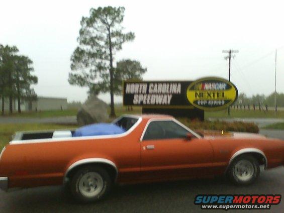 Orange 1979 Ford Ranchero pickup truck parked by a sign for North Carolina Speedway