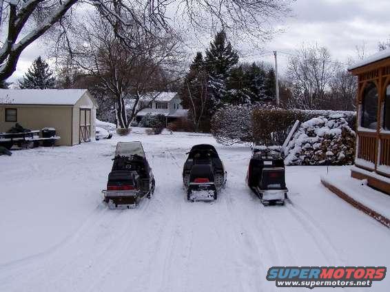 Three snowmobiles parked in a snowy yard