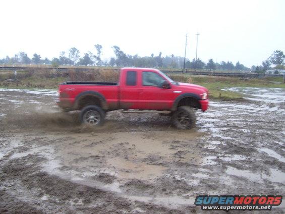 Red pickup truck driving through mud, kicking up spray