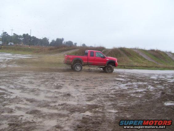 Red pickup truck driving through mud on an overcast day