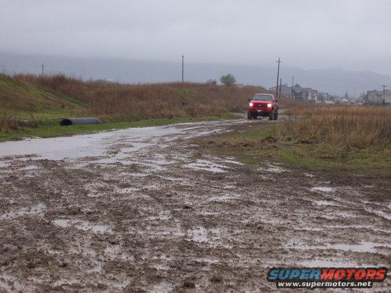 Red pickup truck driving on a very muddy, wet road. Overcast sky