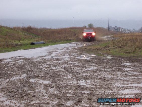 Red truck driving through a muddy field on a cloudy day