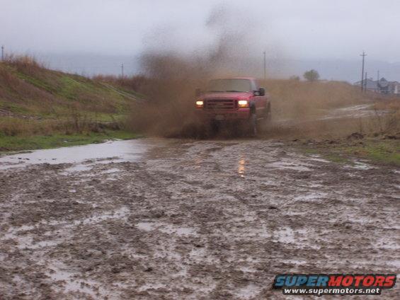Red pickup truck kicking up mud while driving through a muddy road