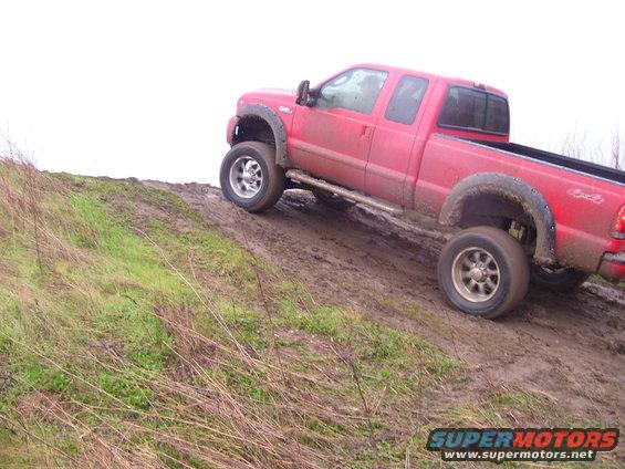 Red pickup truck with fender flares driving up a muddy hill