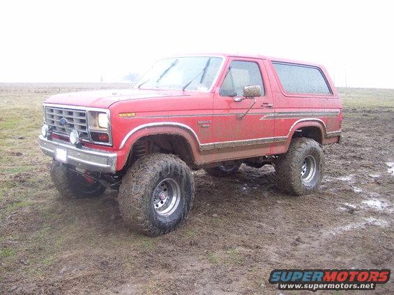 Red lifted Ford Bronco with large tires in muddy terrain