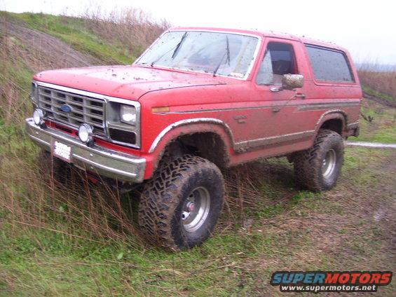 1986 Ford Bronco with large tires on a muddy trail