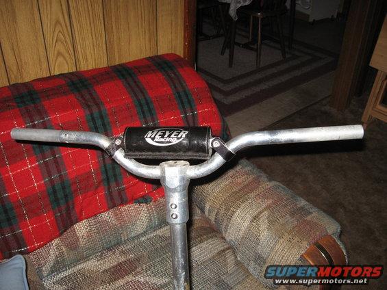 Handlebar with 'Meyer Racing' logo on a metal pole, resting on a plaid blanket and patterned chair