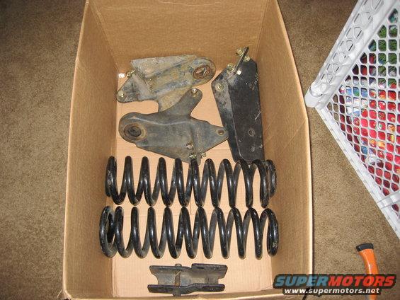 Box of suspension parts, including springs and brackets, on a carpeted floor